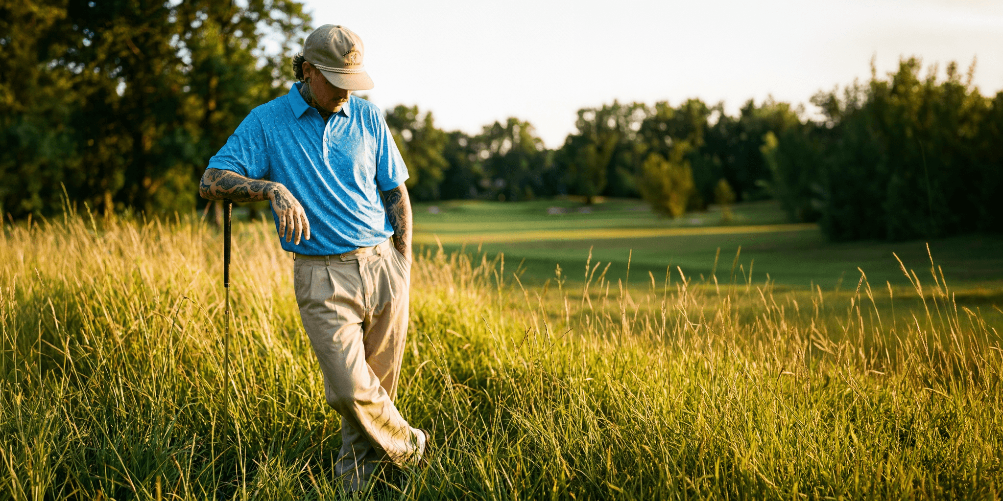 Man walking through tall grass on a golf course with trees in the background