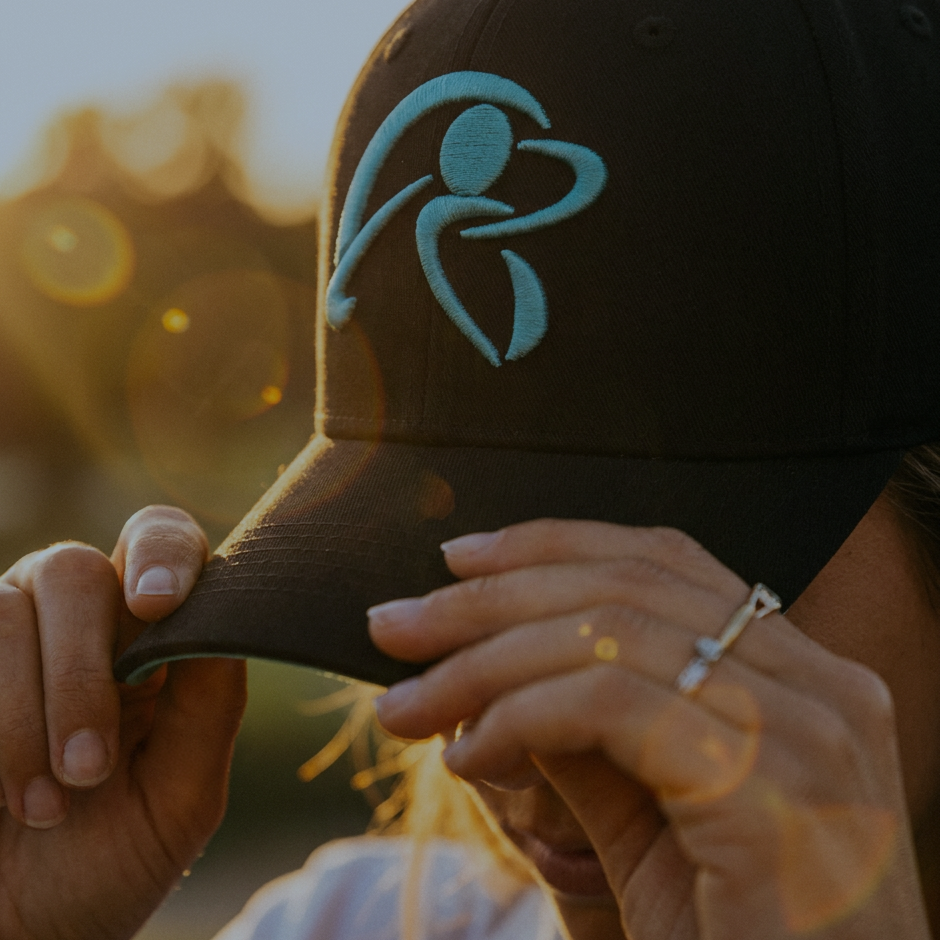 Person holding a cap with a logo against a blurred natural background